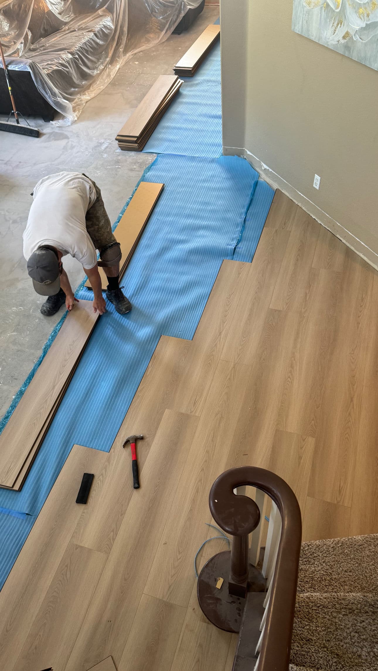 Man installing laminate flooring in a home, with tools and protective covering visible.