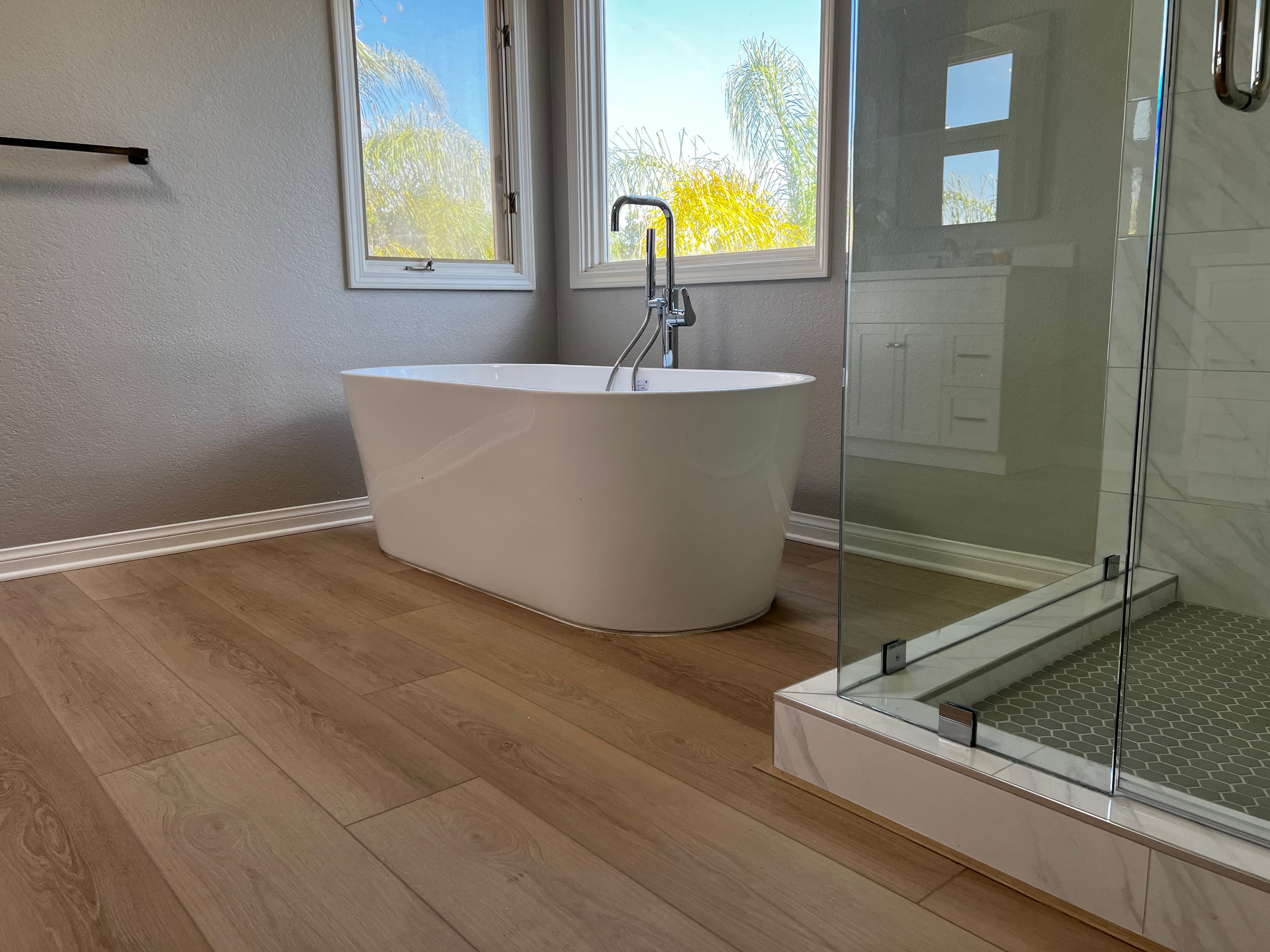 Modern bathroom with freestanding tub, glass shower, and wood-look flooring.