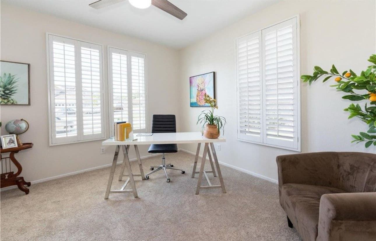 Modern home office with white desk, ergonomic chair, and natural light from shuttered windows.
