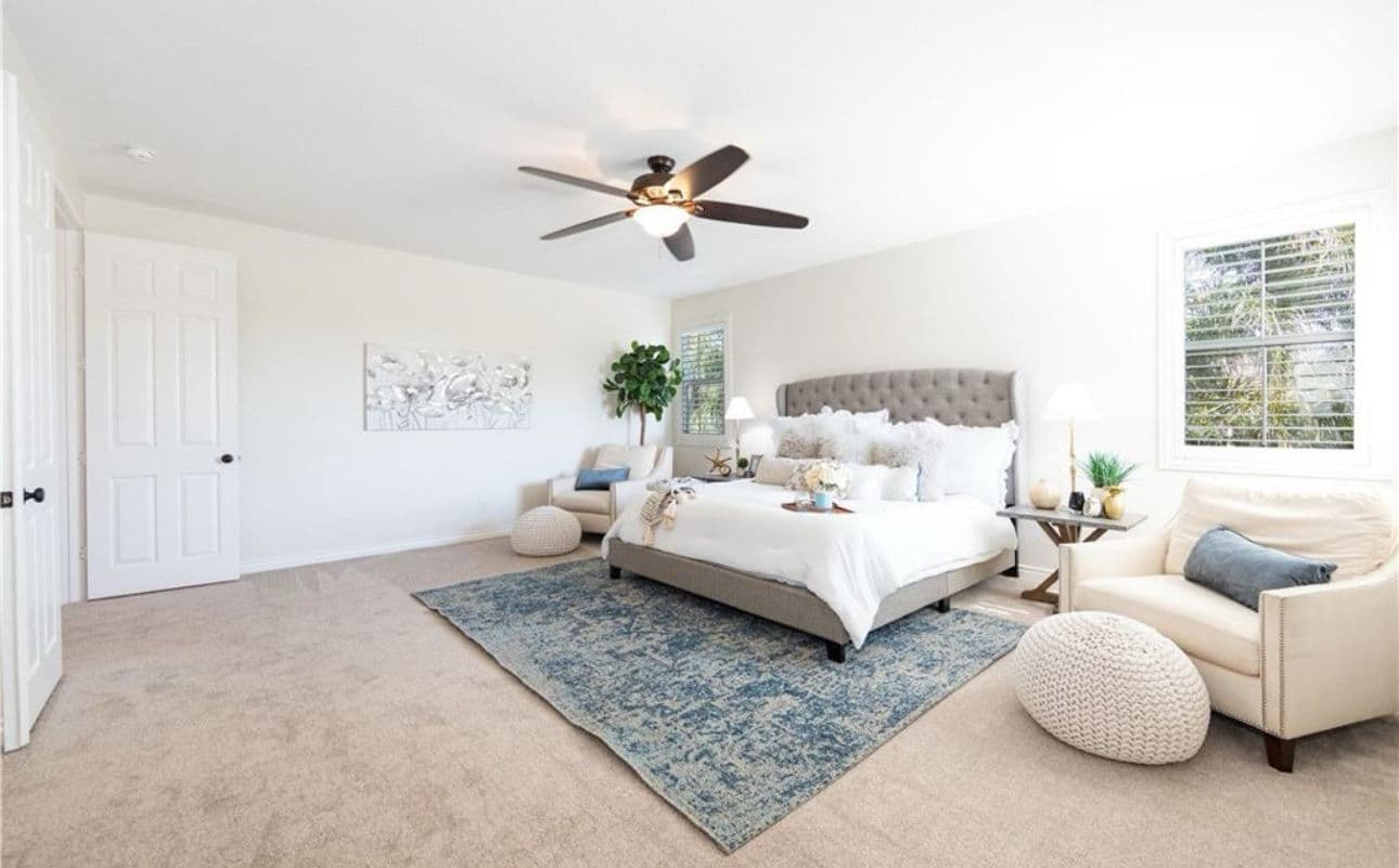 Spacious modern bedroom with a gray upholstered bed, cozy seating, and large windows.