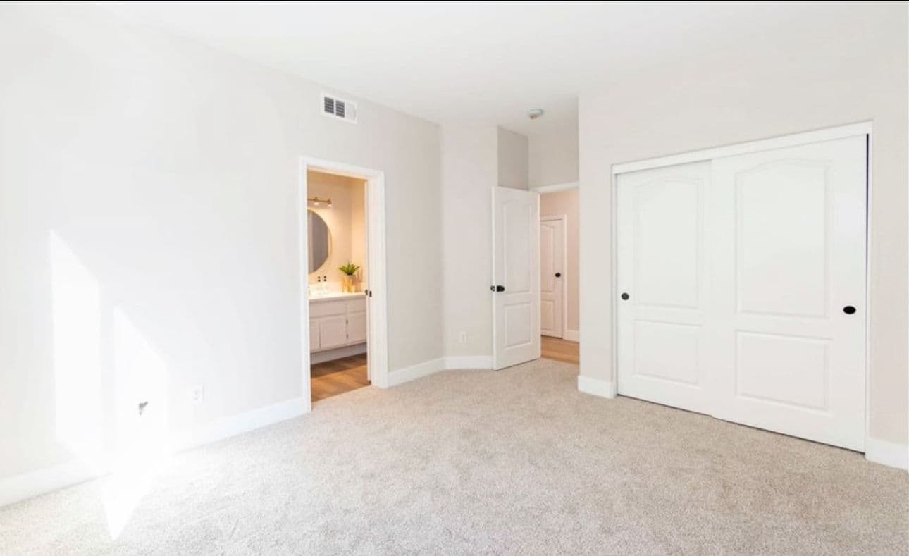 Bright, spacious bedroom with carpet, closet, and adjoining bathroom entrance.