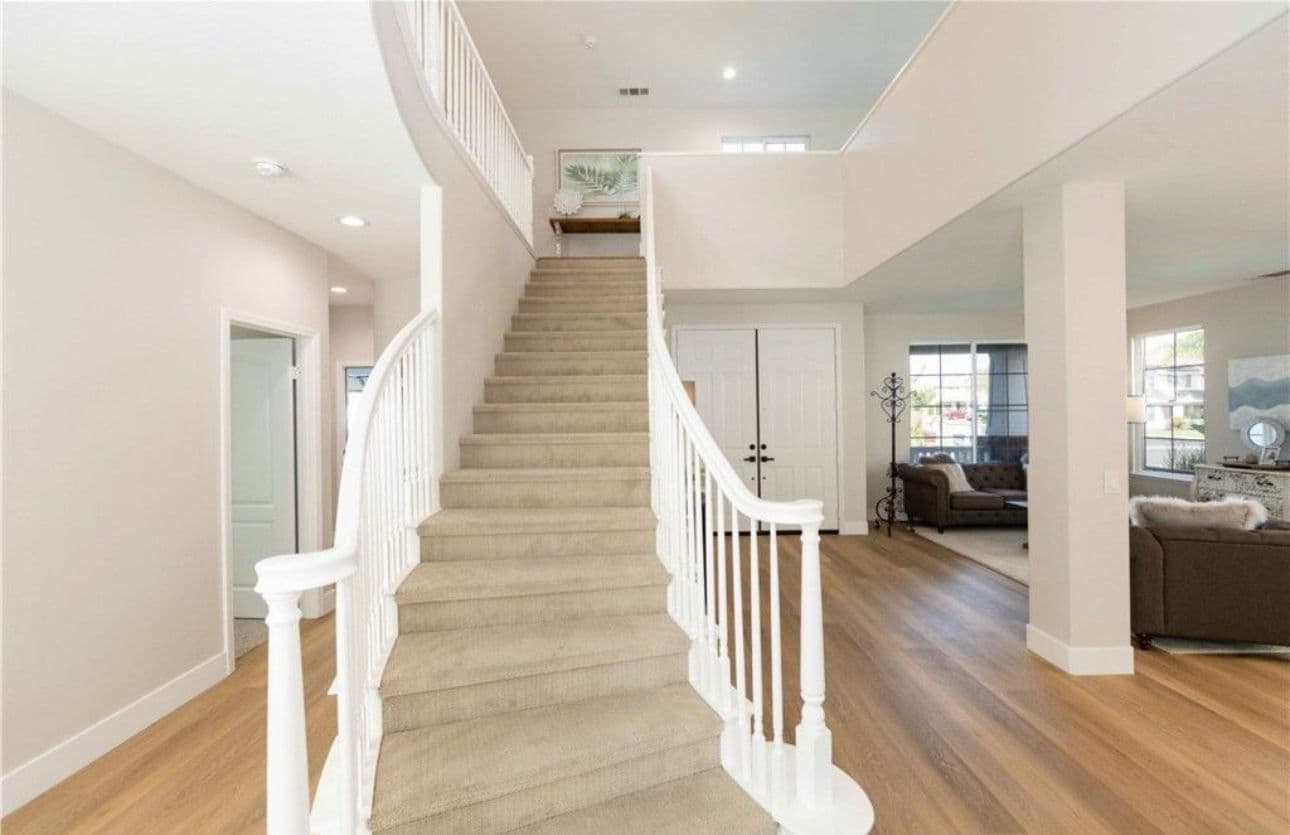 Inviting foyer with a curved staircase and modern decor, featuring natural light and open space.