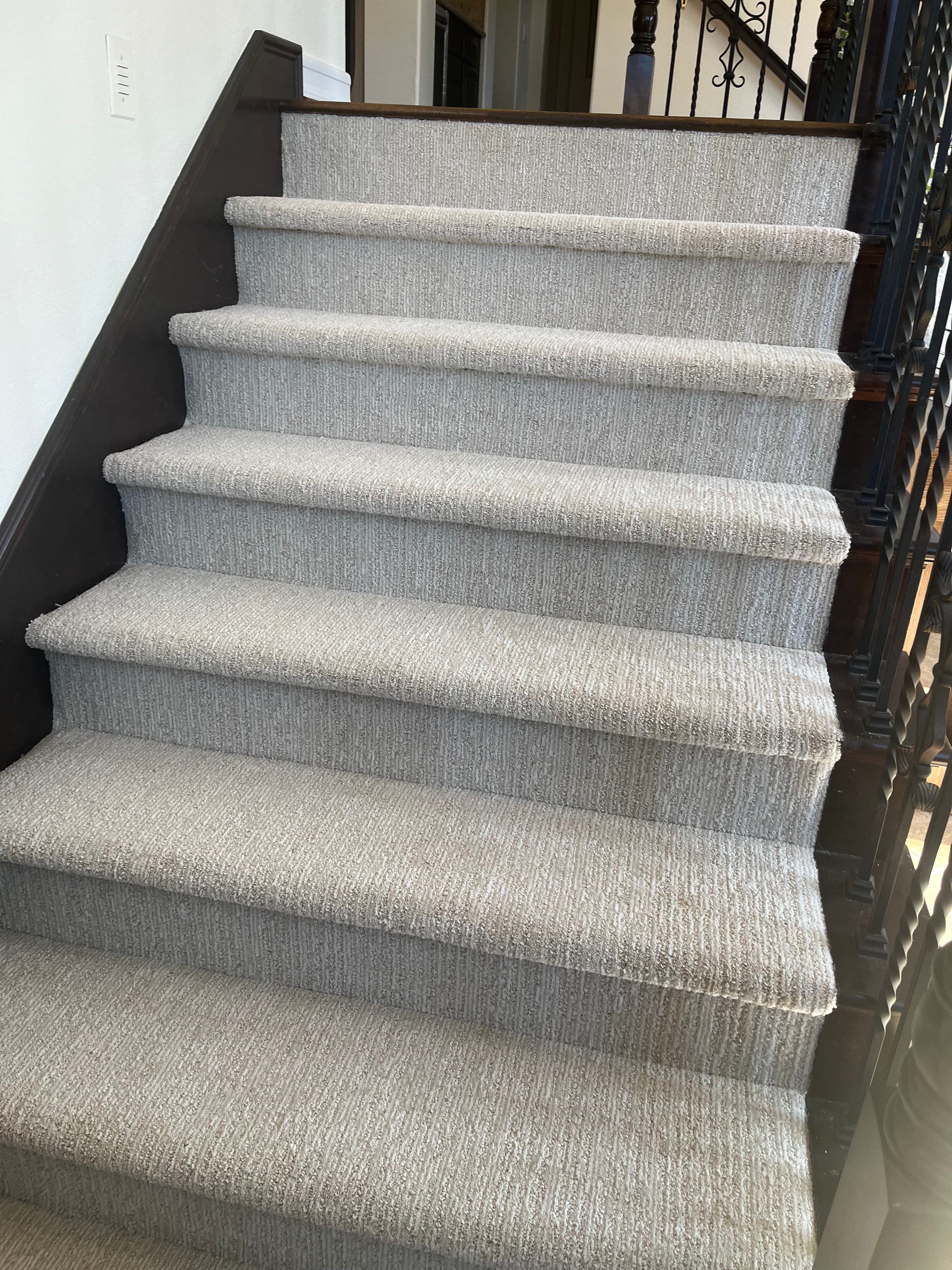 Carpeted staircase with light gray carpeting and dark wooden banister in a modern home.