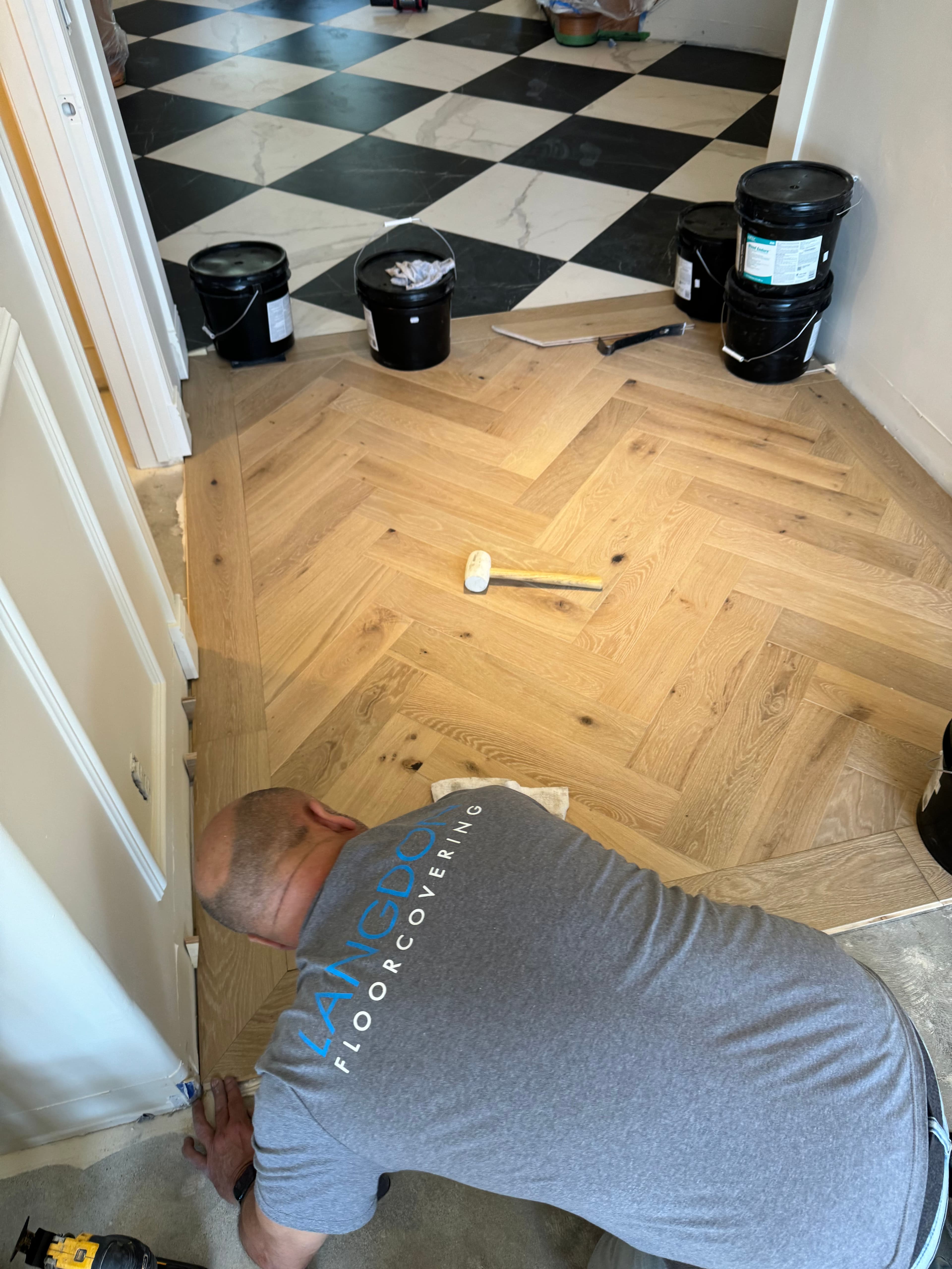 Worker installing herringbone wood flooring in a modern home, surrounded by paint buckets.