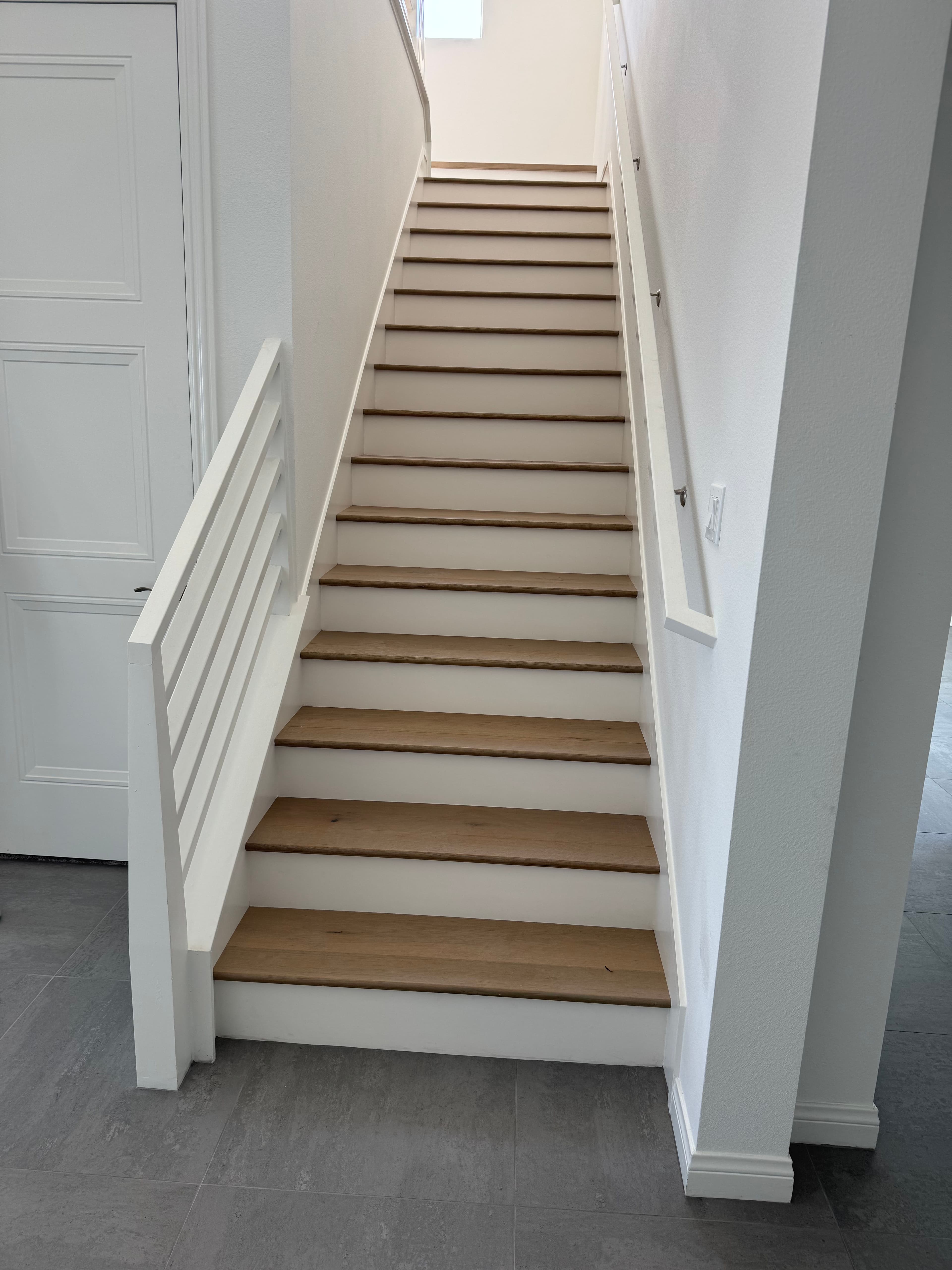 Modern wooden staircase with white railings and light gray tiled floor in bright interior.