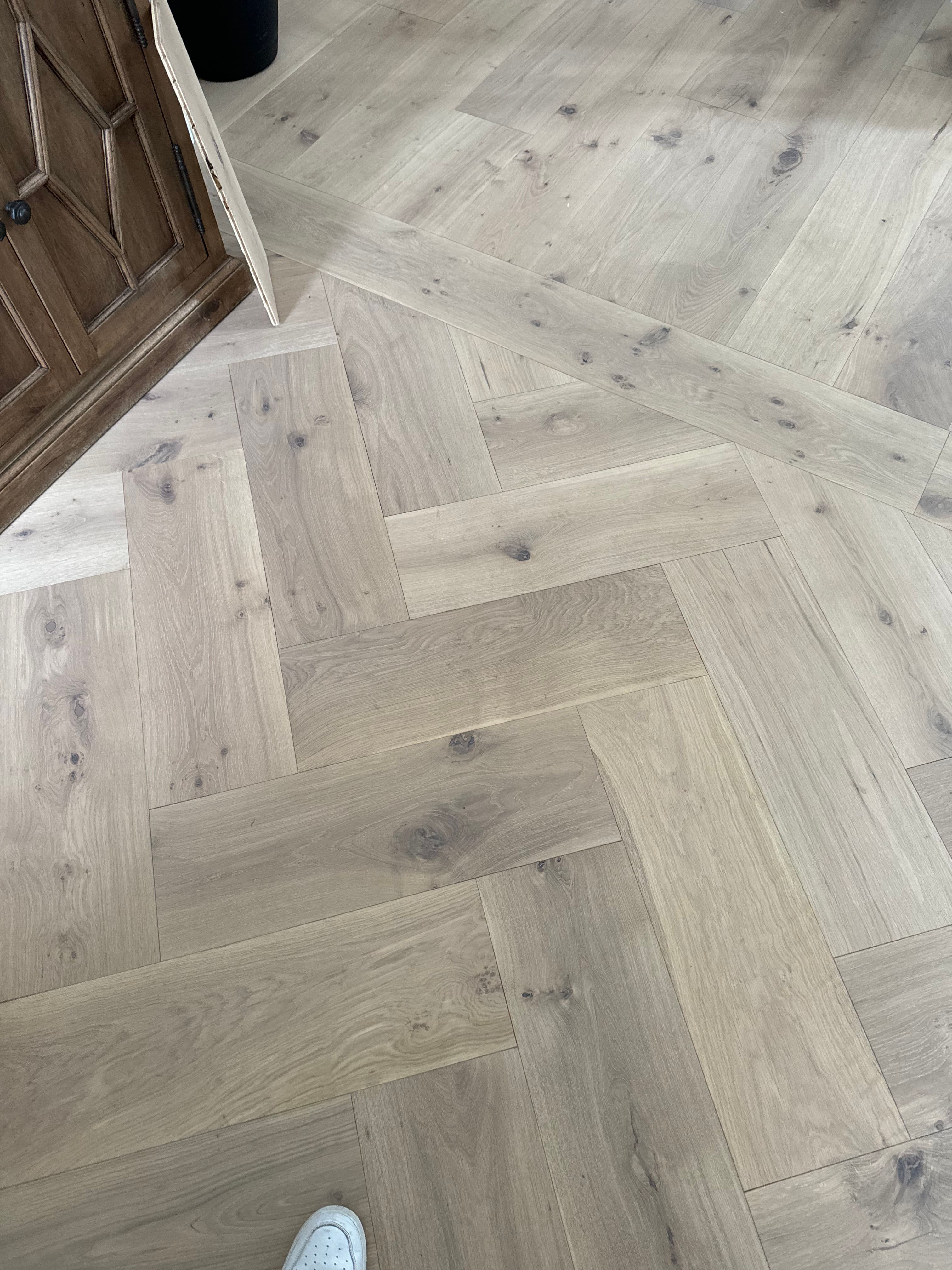 Herringbone pattern hardwood floor with light tones and visible wood grain.