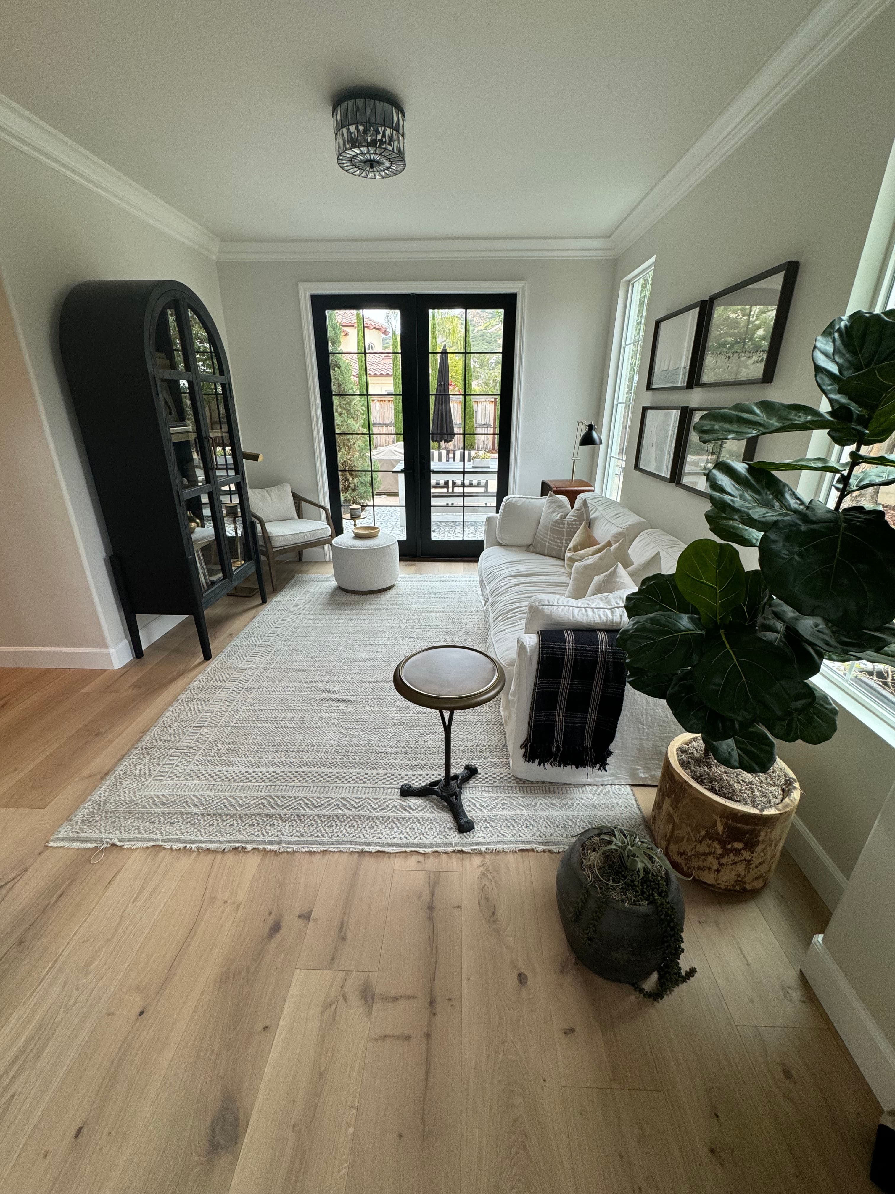 Cozy living room with a white sofa, potted plants, and large windows overlooking a patio.