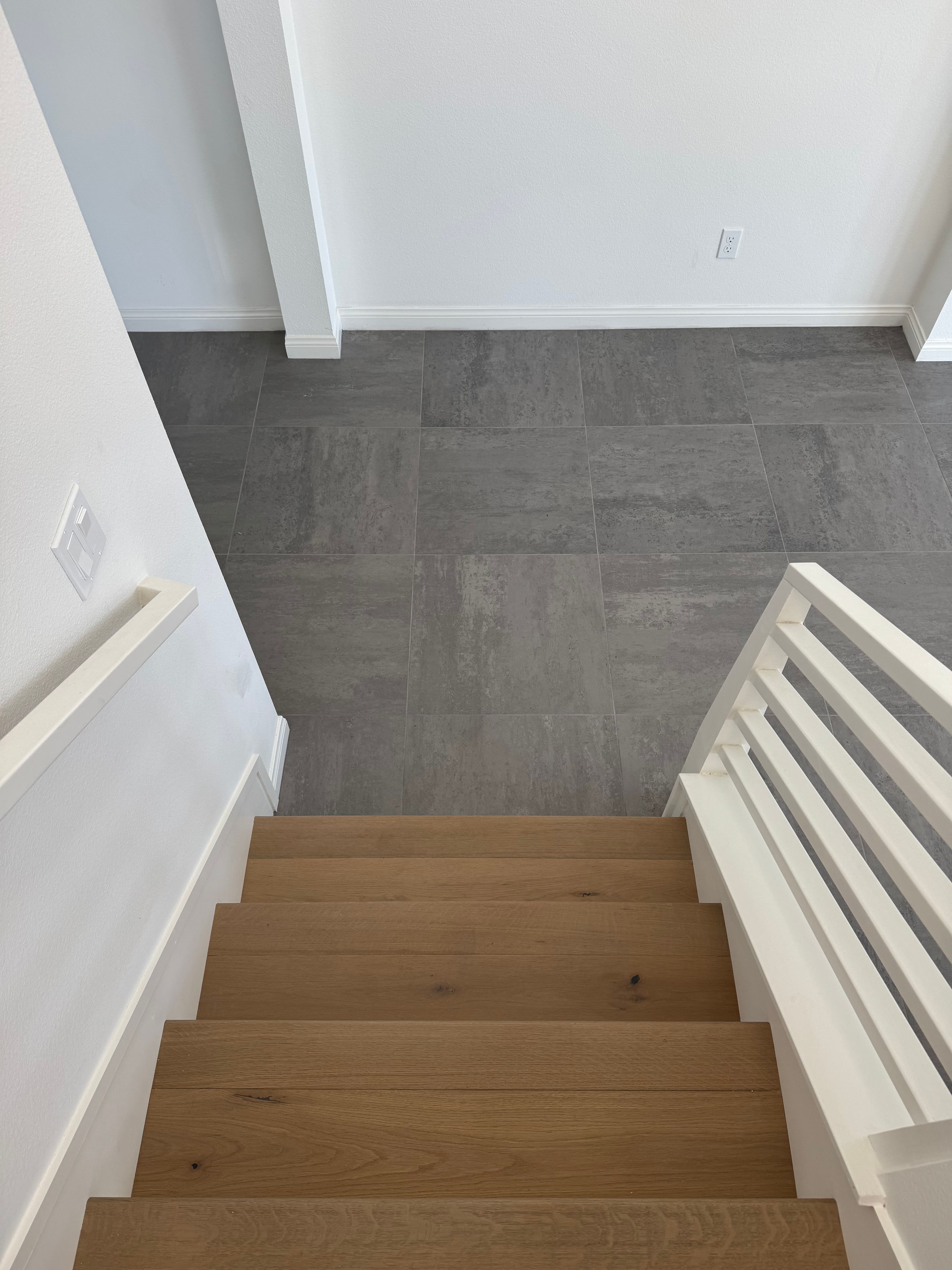 Top view of wooden stairs leading down to a modern tiled floor in a bright room.