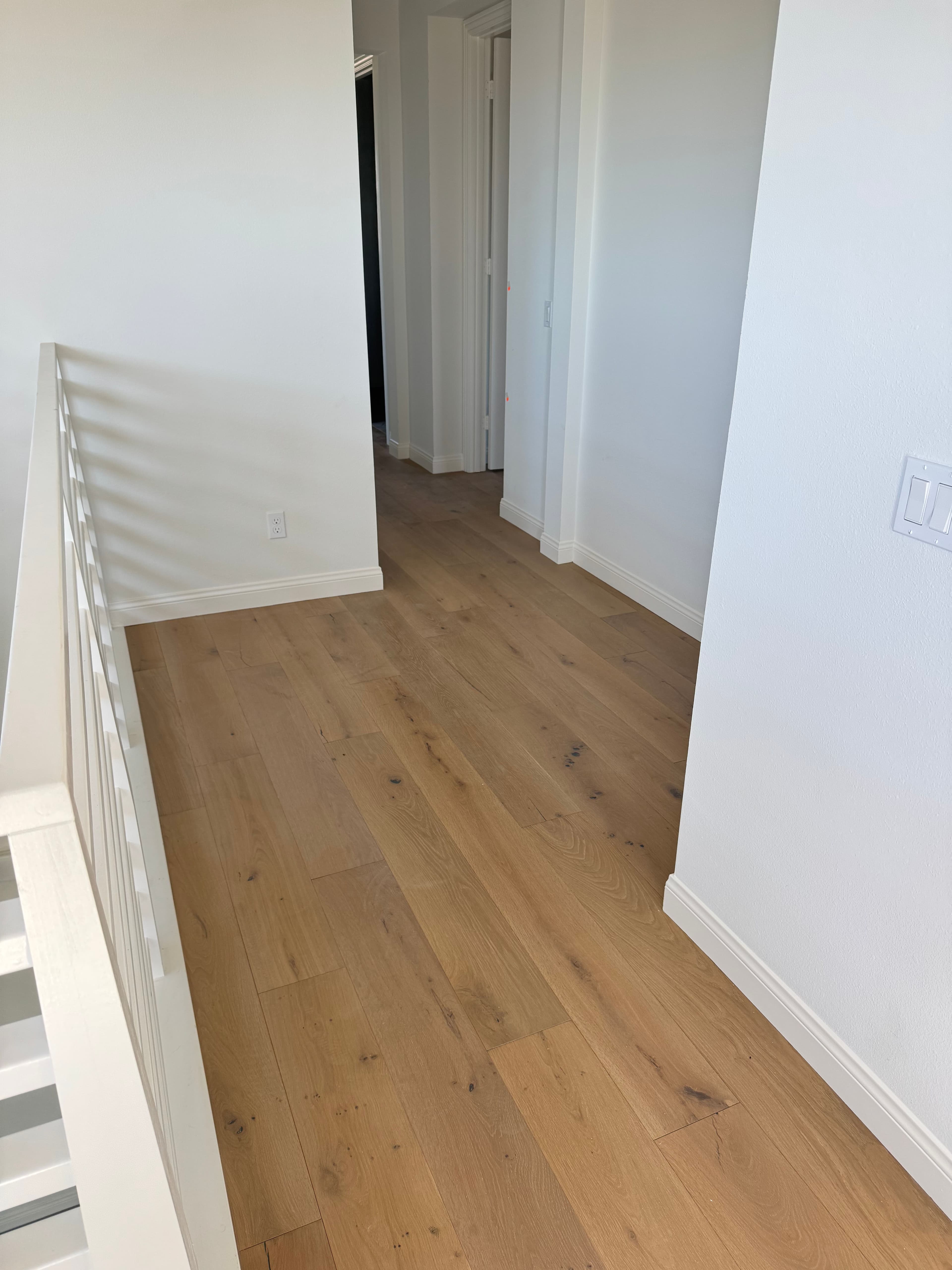 Modern hallway with light wood flooring and white walls, featuring a staircase railing.