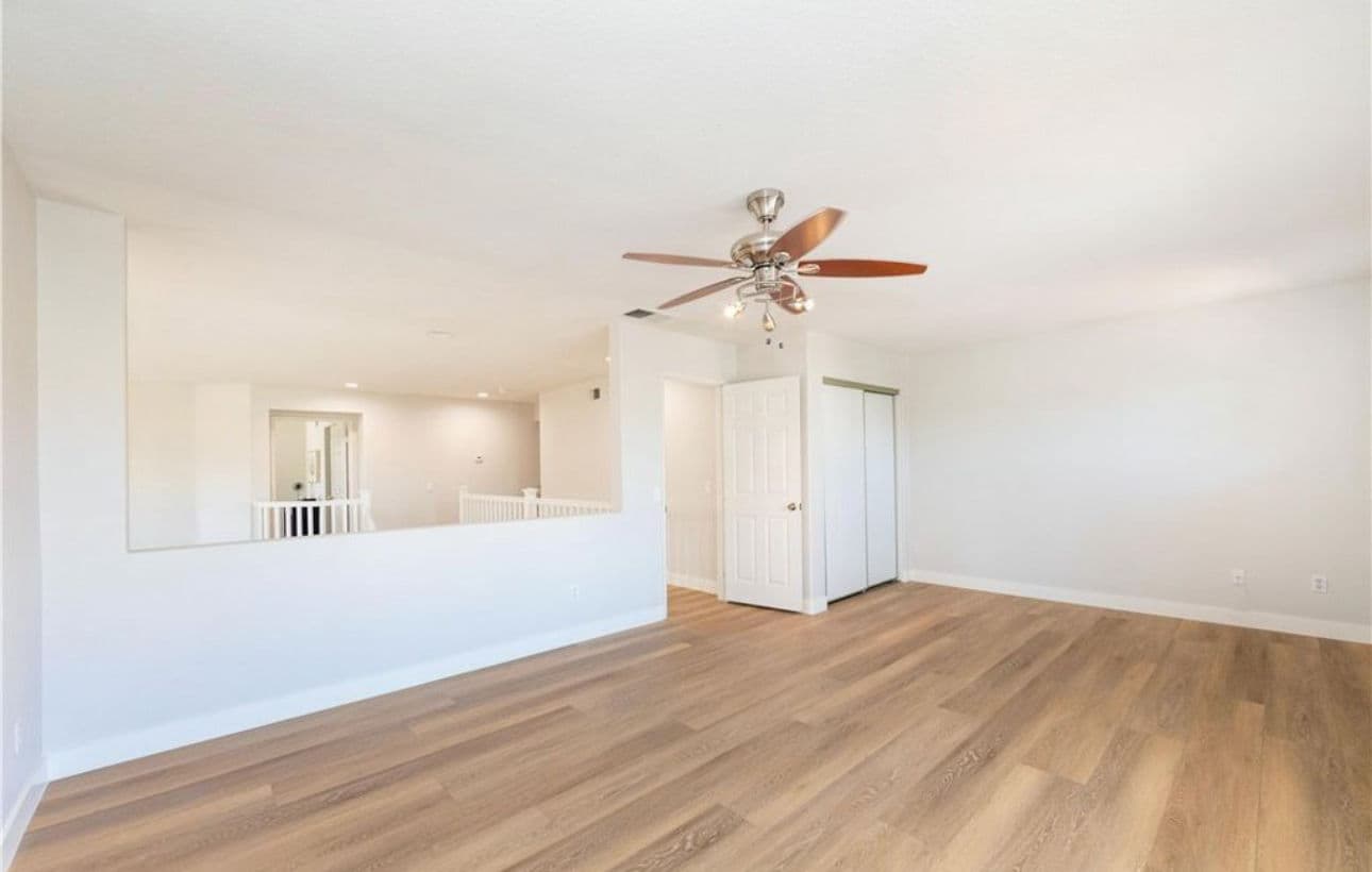 Spacious living area with ceiling fan, light wood flooring, and access to closets.