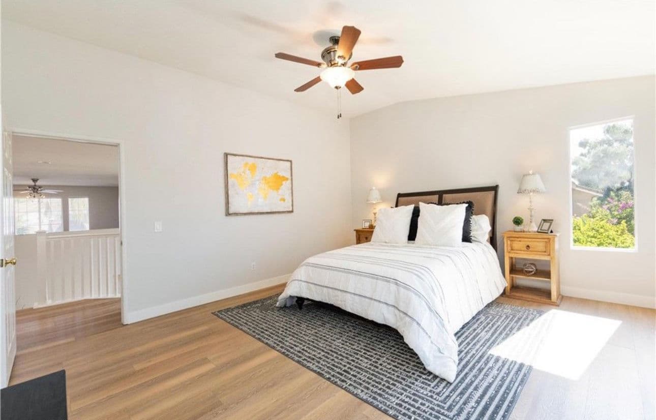 Bright, spacious bedroom with a ceiling fan, queen bed, and natural light from large windows.