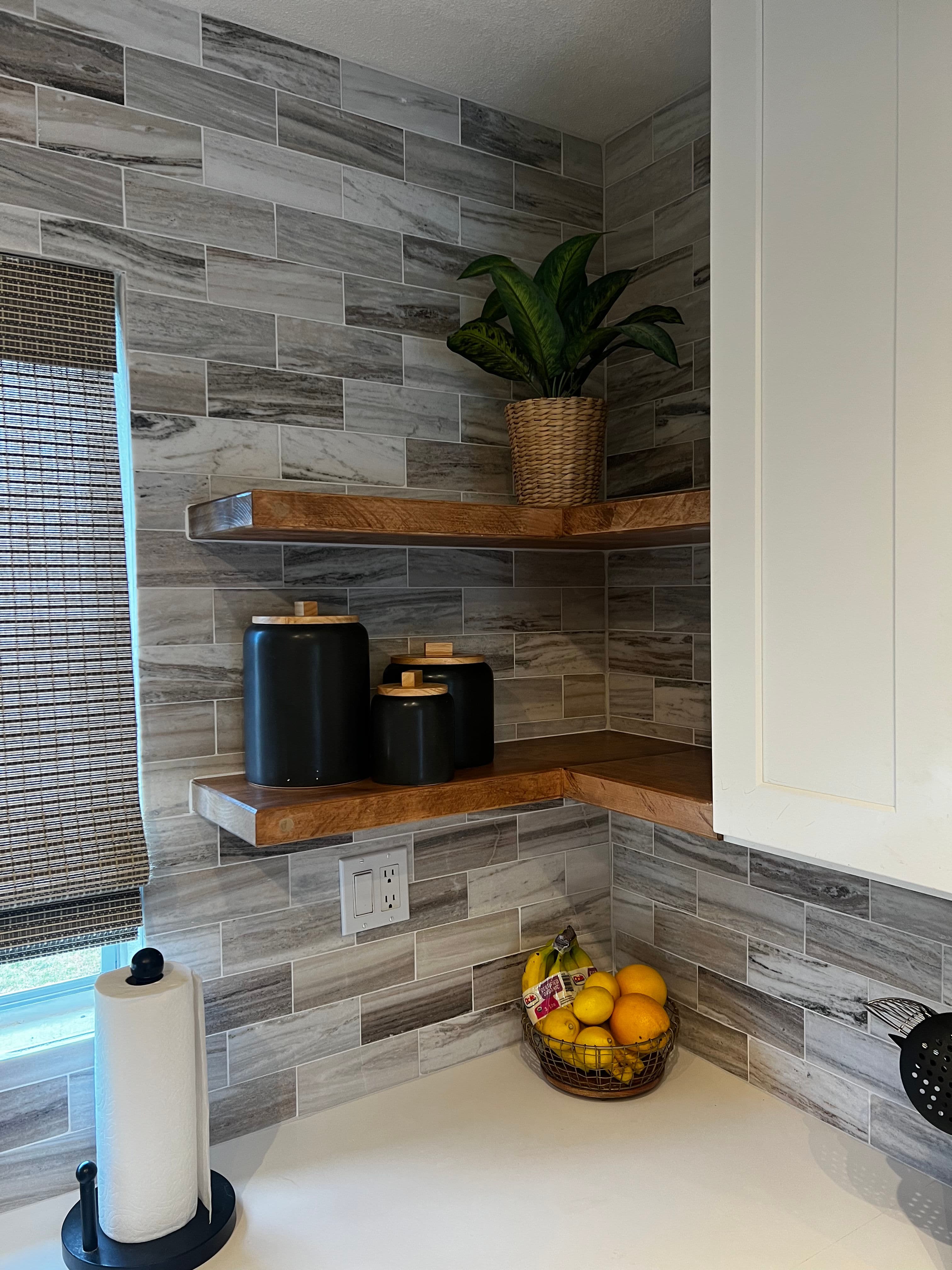 Modern kitchen corner featuring wooden shelves, decorative pots, and a fruit basket.