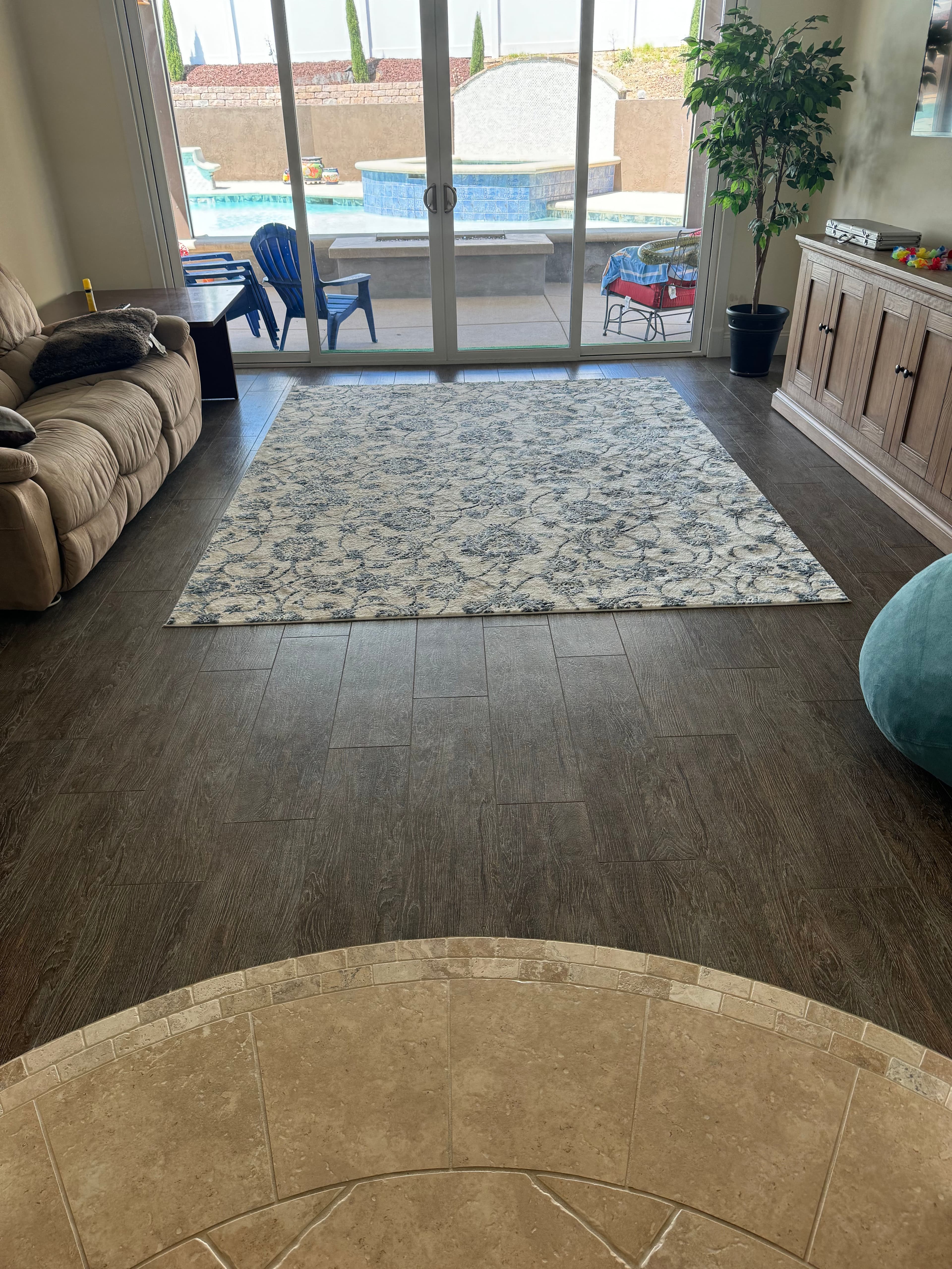 Living room with a large rug, tan sofa, and sliding glass doors overlooking a pool.